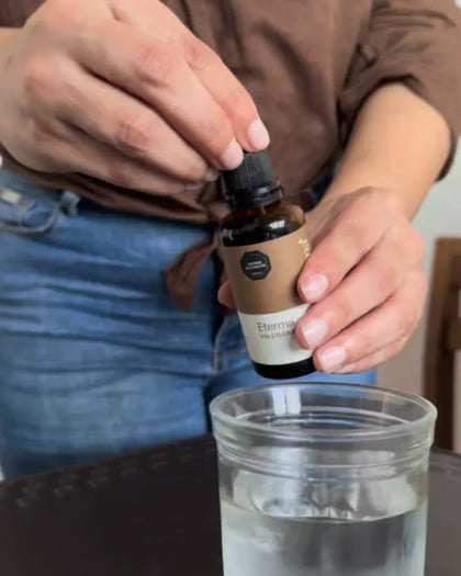 Manos abren el frasco de Valeriana Eterma junto a un vaso de agua